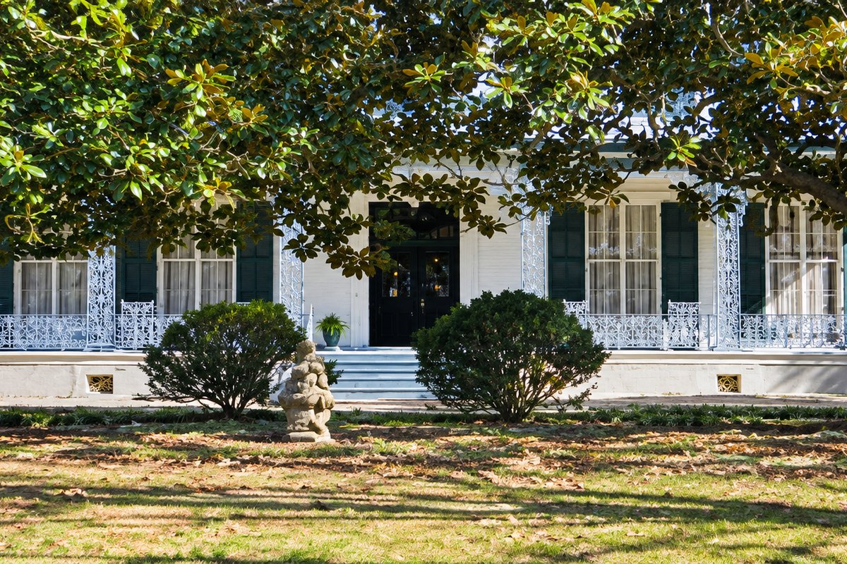 Historic white-columned home shaded by large oak trees